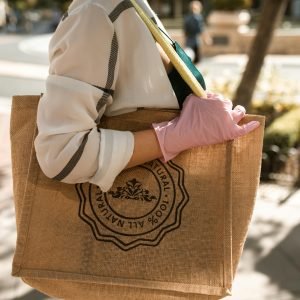 Close-up of a person with a brown tote bag and pink glove, outdoors on a sunny day.