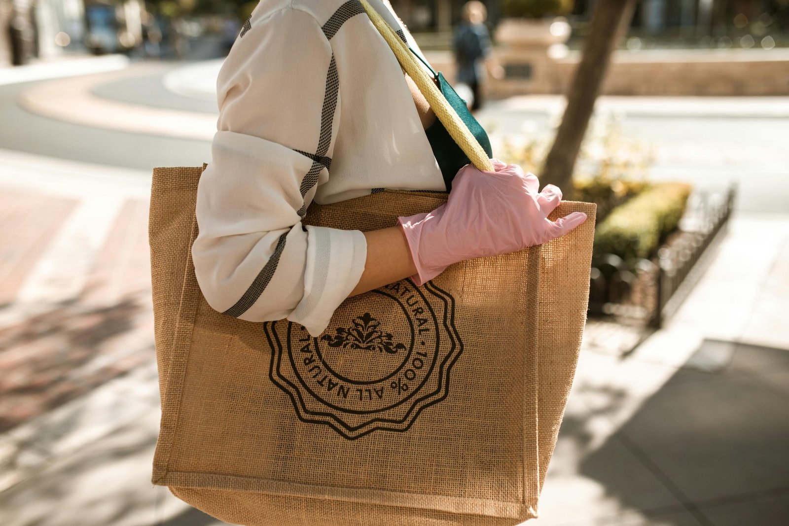Close-up of a person with a brown tote bag and pink glove, outdoors on a sunny day.